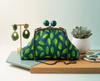 Small clutch purse made from pattern of bright green falling leaves on a deep blue background, with large green wooden balls clasp and chain