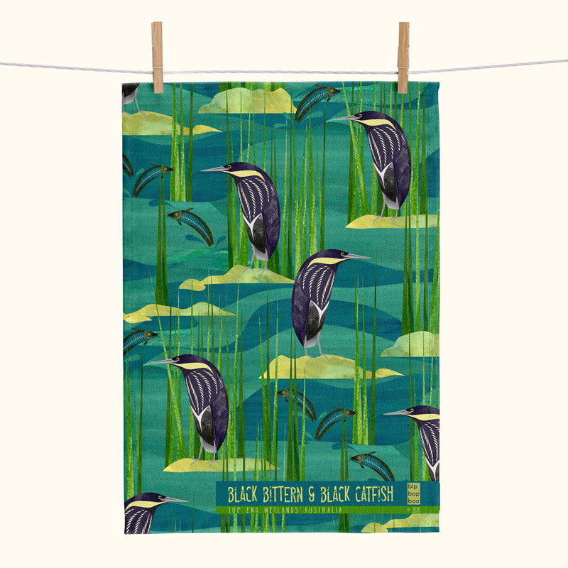 linen tea towel covered with stylised print of black bitterns and black catfish against a watery background with reed and rocks