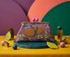 Large clutch purse with purple ball closure. patterned with orange-footed scrub fowls and leaves on a purple background