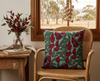 cushion with rosella flowers and leaves on a pale blue-green background on a cane chair by a window