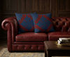 cushion with four large red dragonflies facing  out towards the corners on a dark blue swirly background on a red leather couch