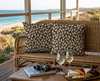 two cushions patterned with stylised tufted grass heads against a brown spotted background on a couch on a beach-side verandah