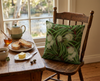 cushion cover with river red gum pattern with leaves and cream blossoms on a dark green background on a timber chair at a breakfast table