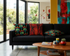 cushions featuring a pattern of red-tailed black cockatoos on wattle branches and an orange pandanus cushion on a black couch in a modern house