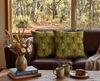Two cushions featuring highly stylised silver-crowned friarbirds on a green leaf-like pattern on a brown leather couch