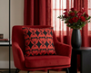 cushion patterned with Sturt's desert pea flowers against black diamonds set in red ovals on a red background on a red velvet chair