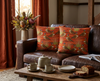 45cm square cushion featuring a pattern of spinifex pigeons and pigeons against an orange desert theme background on brown leather couch