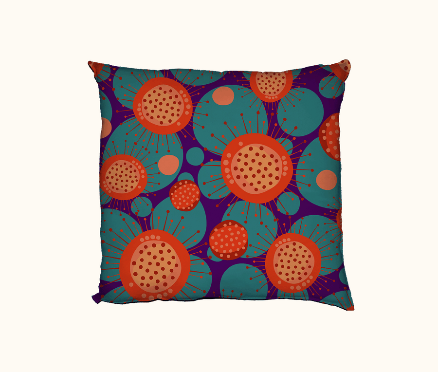 cushion with a bright abstract sundew pattern in reds and oranges, against a background of large irregular spots of teal on purple
