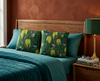 cushions with stylised repeat pattern of superb fairywrens in a flowering banksia marginata on a bed with teal bedclothes