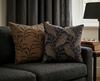 Brown cushion cover with a simple black leaf design on a couch with a tawny frog mouth cushion