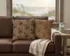 two cushions - one beige and tan and one beige and brown with green highlights -  featuring a repeat pattern of Minoan-inspired octopi and fish in a lounge room with windows looking out on a beach