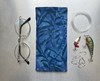 Canvas glasses slip case featuring a leafy pattern of deep sea kelp with bubbles in blue pictured with glasses and fishing equipment.
