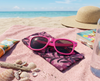 Canvas glasses slip case featuring a leafy pattern of deep sea kelp with bubbles in pinks and purples lying on a pink towel on a beach with pink sunglasses, shells, sunblock and a sunhat