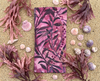 Canvas glasses slip case featuring a leafy pattern of deep sea kelp with bubbles in pinks and purples lying on sand surrounded by pink kelp and sea shells