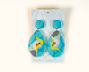 acrylic drop earrings featuring stylised cockatiels, one the right way up and one upside down
