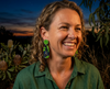 A woman wearing acrylic earrings featuring flying foxes hanging upside down among bright green leaves