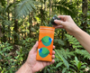 Canvas glasses slip case featuring very round and highly stylised blue-faced parrotfinches on an orange background with a pair of green glasses being removed from them against a tropical forest background