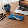 Canvas glasses slip case featuring a pop art bush stone curlew on a striped blue background sitting on a desk with a laptop, a cup of coffee and a selection of pens