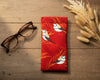 Canvas glasses slip case with stylised double barred finches with red and gold grasses on a red background