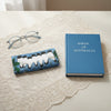 Canvas glasses slip case featuring stylised white breasted woodswallows bunched up together sitting on a branch against a blue pattern of leaves.