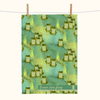 a linen teatowel featuring stylised green tree frogs on a watery green background with some small clumps of grass