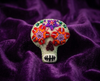 Very pale green sugar skull felt brooch with red and orange eyes and a purple star on the forehead