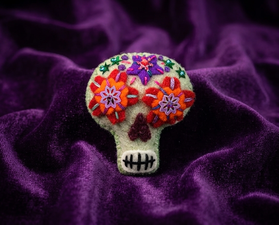 Very pale green sugar skull felt brooch with red and orange eyes and a purple star on the forehead