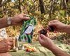 Canvas glasses slip case featuring a laughing kookaburra in a flowering river red gum being held by a man's hand while another man holds a pair of red sunglasses in his hands against a picnic in the Australian bush