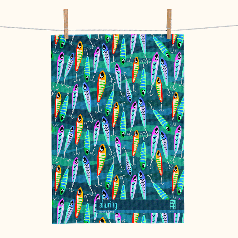 a linen tea towel printed with a pattern of colourful lures against blue and green waves