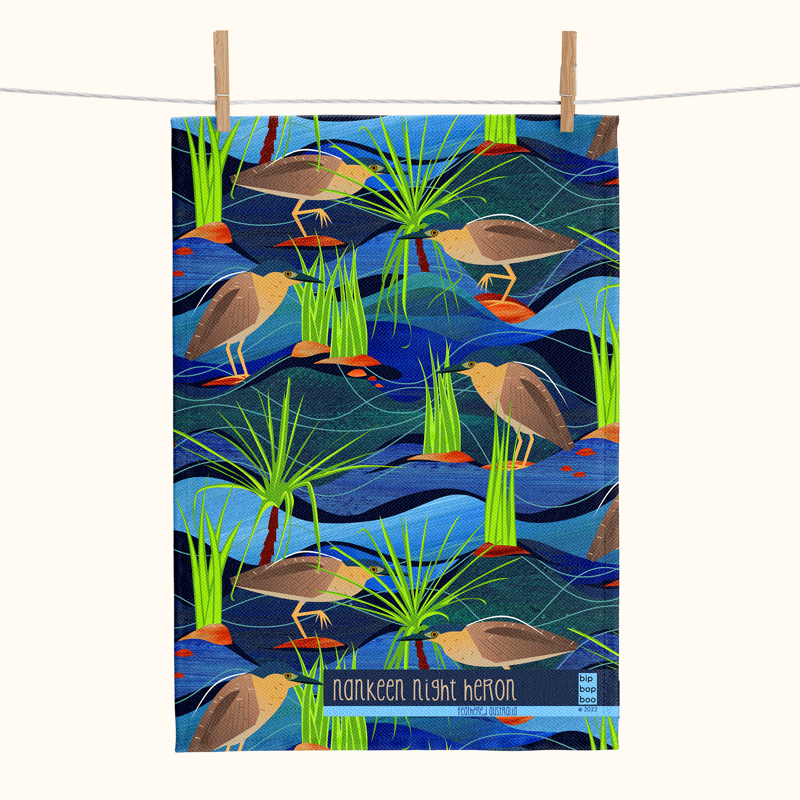 linen tea towel featuring a stylised pattern of Nankeen night herons in a blue stream with rocks, reeds and pandanus
