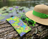 Canvas glasses slip case featuring a pattern of striped rocket frogs on waterlily pads with purple waterlily  flowers on a log with a pair of green glasses, and a sunhat