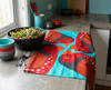 linen tea towel showing four large stylised crimson finches on a pale teal green background draped on a bench with a salad and bowls