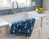 linen tea towel covered in grass pattern and double-barred finches on a blue background draped on a sink in a white kitchen