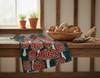 linen tea towel showing red and white spotted mushrooms on a timber bench with a bowl of mushrooms and a garden trowel