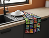 a brightly coloured linen teatowel with highly stylised and very round finches in squares lying on a bench near some dishes on a draining board