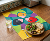 bright linen tea towel with three large stylised Gouldian finches against a green background on a kitchen bench with a plate of salad and bread