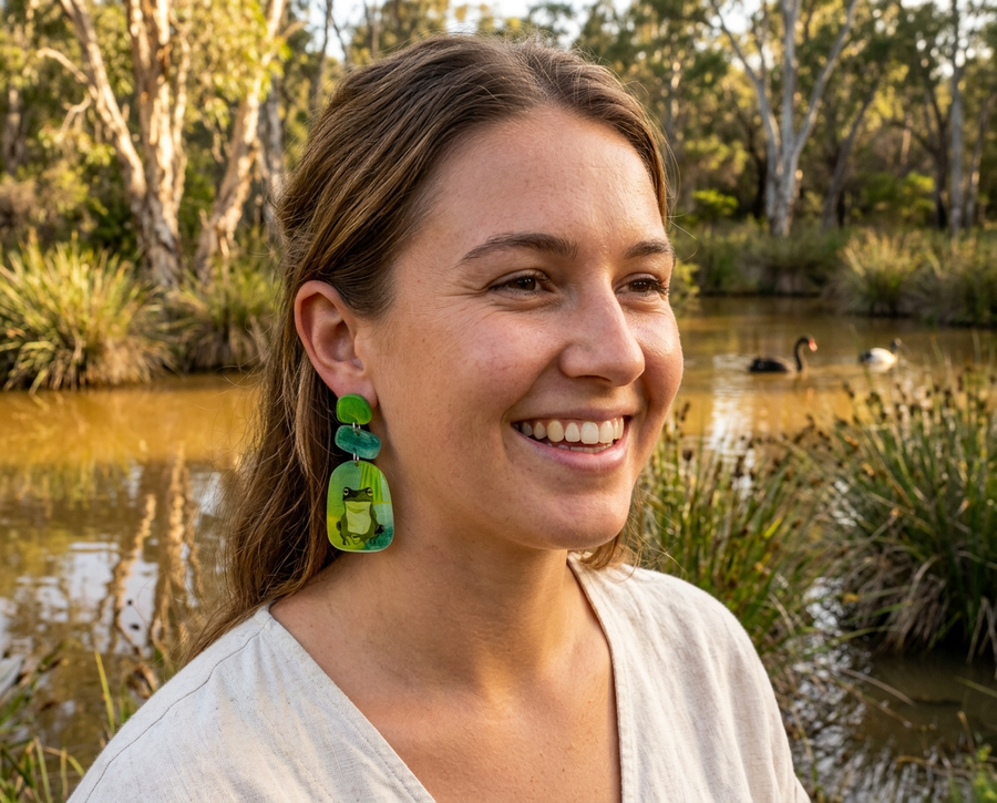 a woman wearing acrylic drop earrings featuring green tree frogs