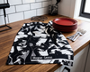 black and white linen tea towel covered with magpie geese lying on a kitchen bench with some red plates