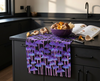 linen tea towel printed with rows of tall purple mushrooms against a black background on a kitchen book with a bowl of mushrooms and a mushroom identification book