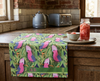 linen tea towel printed with an overall pattern of pink and grey galahs against a backdrop of gum leaves draped on a bench in a rustic kitchen