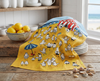 A tea towel showing a beach scene of cartoon birds engaged in festival activities draped over a stack of plates in a beach house kitchen