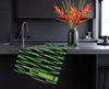 a linen tea towel featuring bright green stylised freshwater crocodiles on a black background on a kitchen bench next to a vase of heliconia flowers